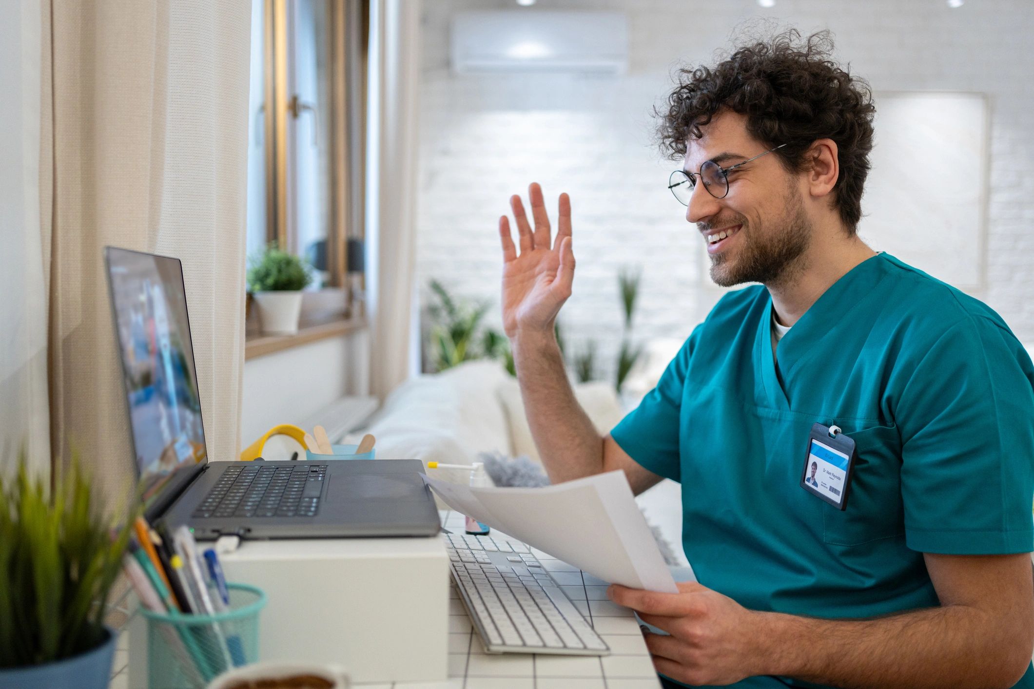 Male nurse in scrubs, waving back to a patient during a video call